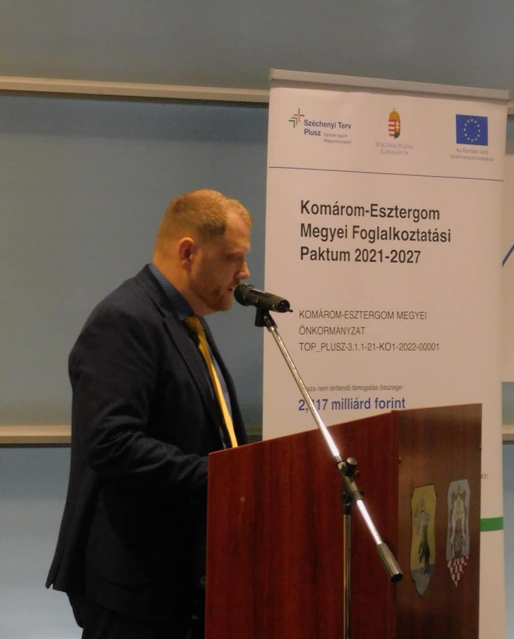 Előadó beszél pódiumról, mellette információs Roll-up.