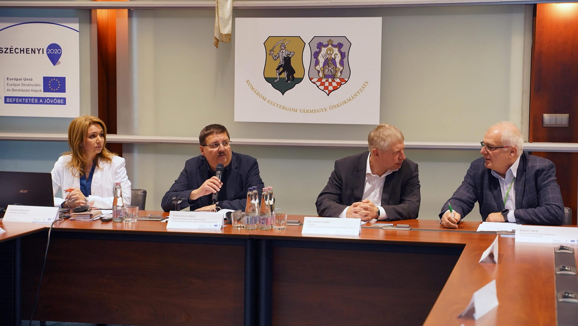 Popovics György elnök és Kancz Csaba főispán ülnek az elnökségi asztalnál, előttük dokumentumok.”