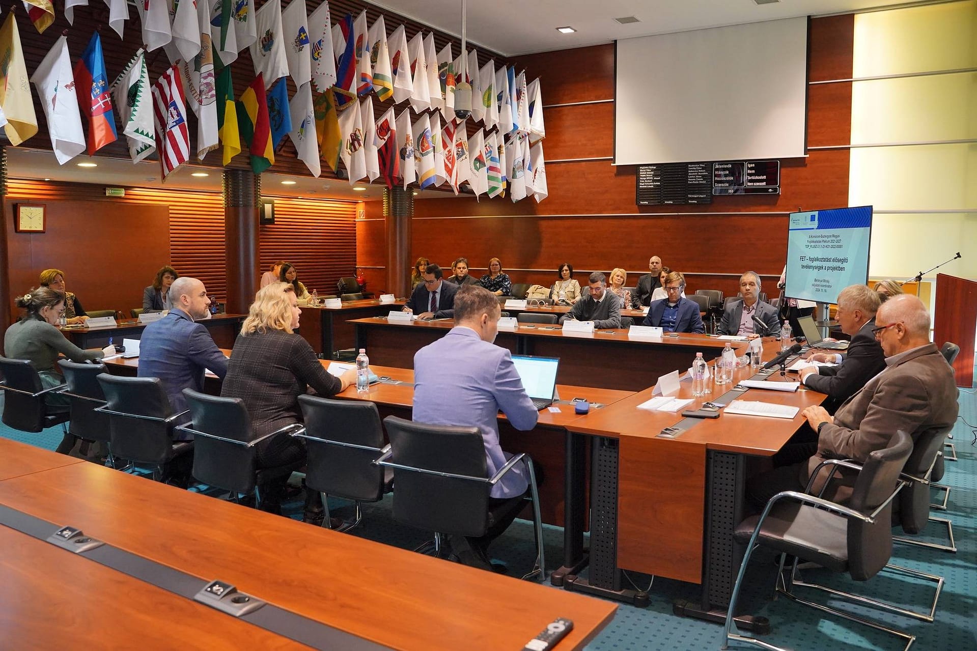 Szakmai egyeztetés egy modern konferenciateremben, a résztvevők tárgyalóasztal körül ülnek.