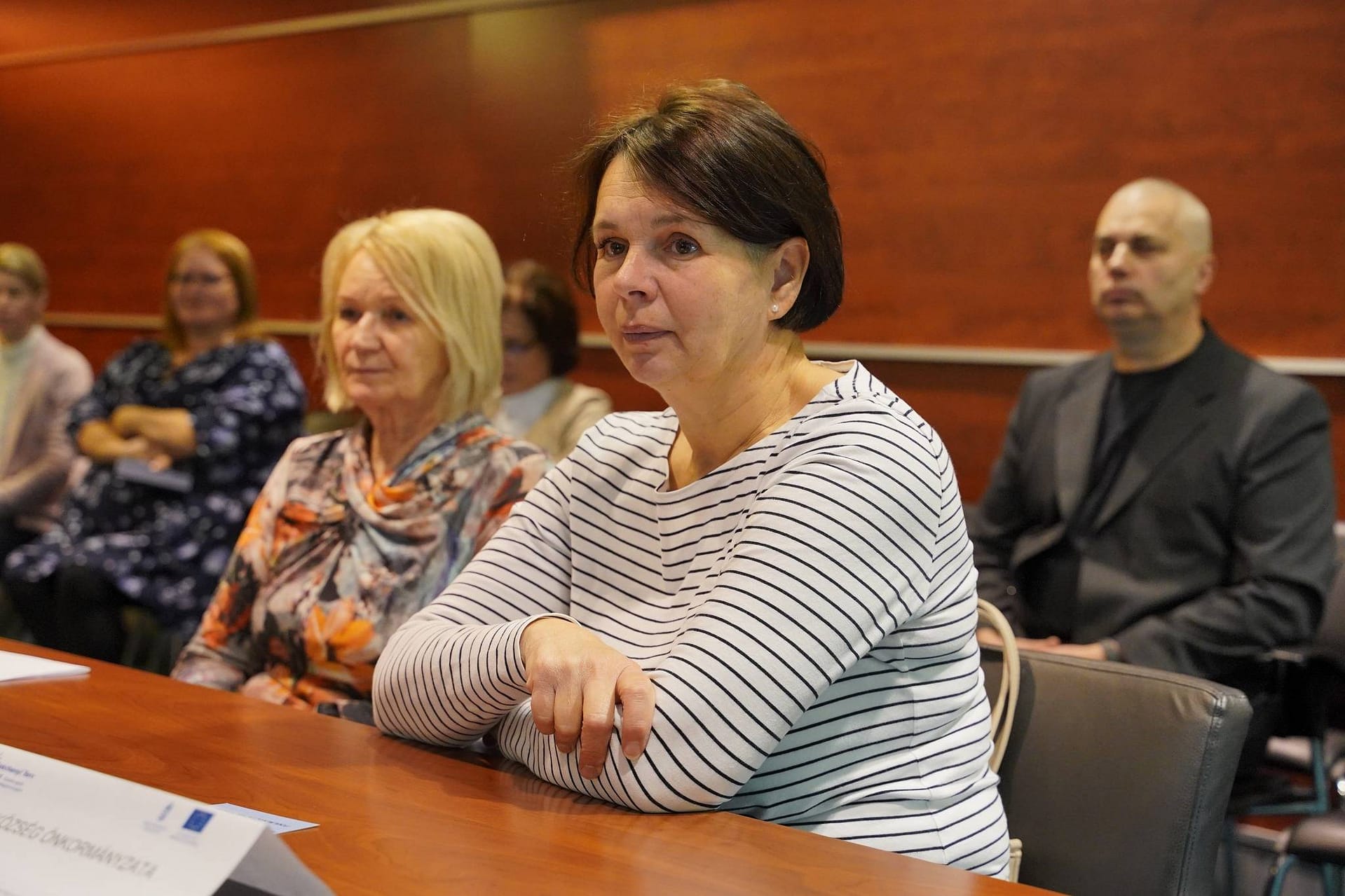 Résztvevők egy szakmai fórumon, az előtérben hallgatóság figyelmes arckifejezéssel.