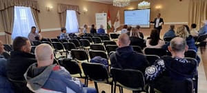 Előadás közbeni pillanat, a közönség figyelme a vetítővászonra és az előadóra irányul.