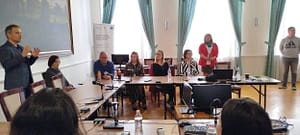 Panelbeszélgetés egy asztalnál, a résztvevők jegyzetek és dokumentumok mellett egyeztetnek.