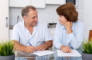 Idős házaspár otthon asztalnál ülve dokumentumokat néz