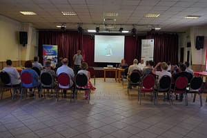 Előadás egy közösségi teremben, a hallgatóság a kivetített prezentációt figyeli.