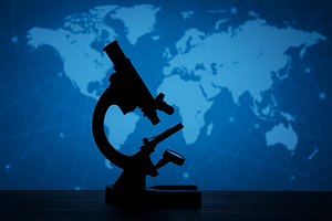 Sötét sziluettű mikroszkóp áll egy asztalon, a háttérben kék világatlasz és hálózati kapcsolati vonalak láthatók.
